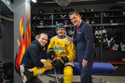 Ein Mann hält das Bein eines Hockeyspielers und daneben steht Stadtrat Peter Hanke